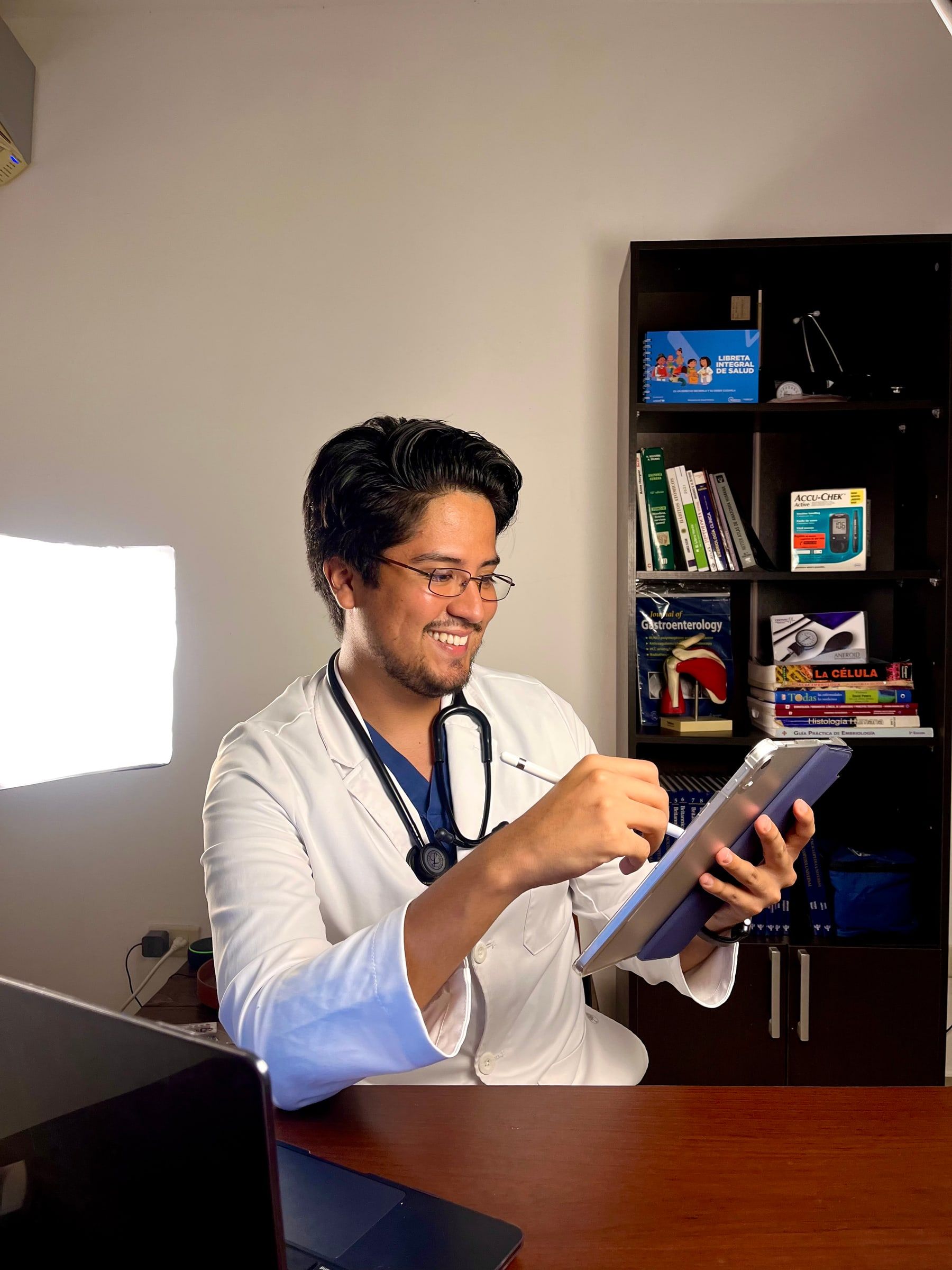 Javier con bata blanca revisando información en una tablet, en su consultorio.